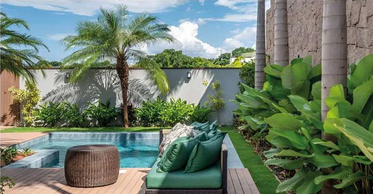 Deck em área de lazer com piscina, sofá verde e jardim tropical