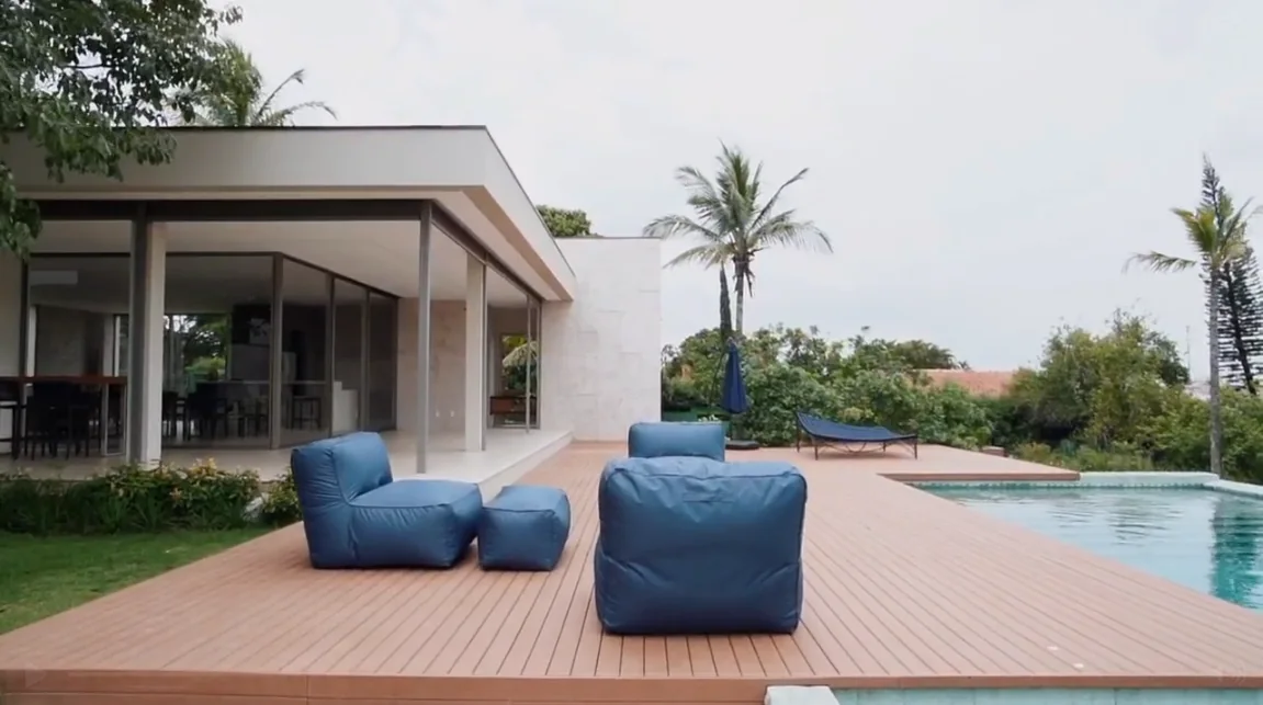 Casa contemporânea com poltronas azuis sobre deck de madeira ecológica, piscina e jardim