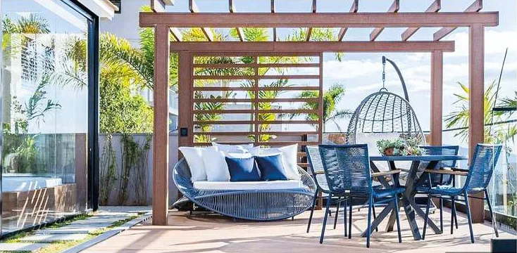 Pergolado com mesa de jantar e balanço sobre deck junto à piscina